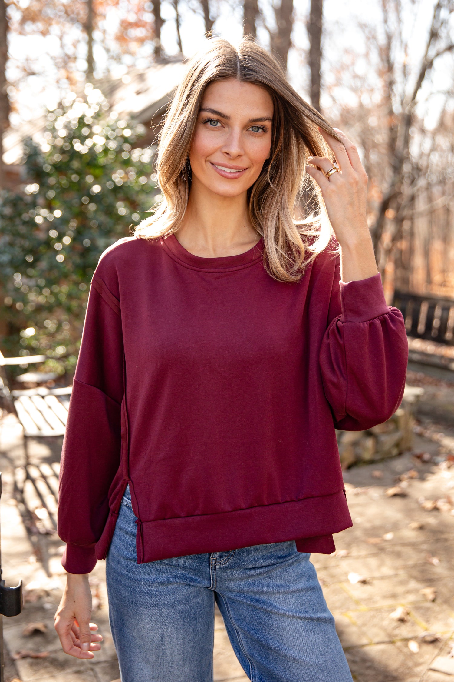 Woman wearing a maroon sweatshirt and blue jeans outdoors