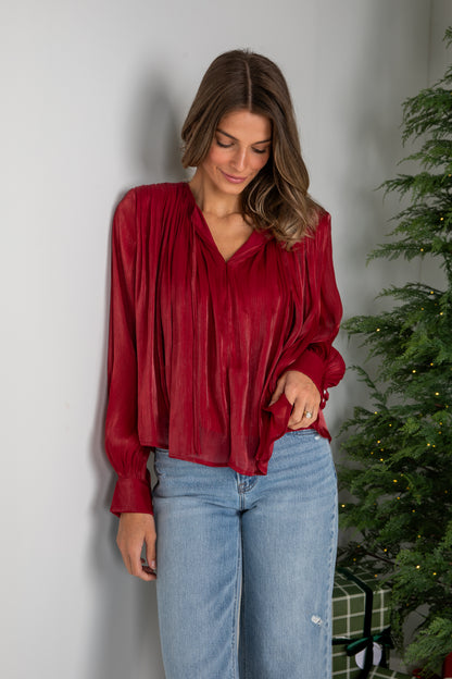 Woman wearing a red blouse and blue jeans standing next to a Christmas tree.