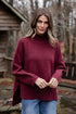 Woman wearing a maroon sweater outdoors with a wooden cabin in the background