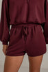 A close-up of a person wearing a matching burgundy lounge set, featuring a cropped long-sleeve top and high-waisted shorts with an elastic drawstring waist.