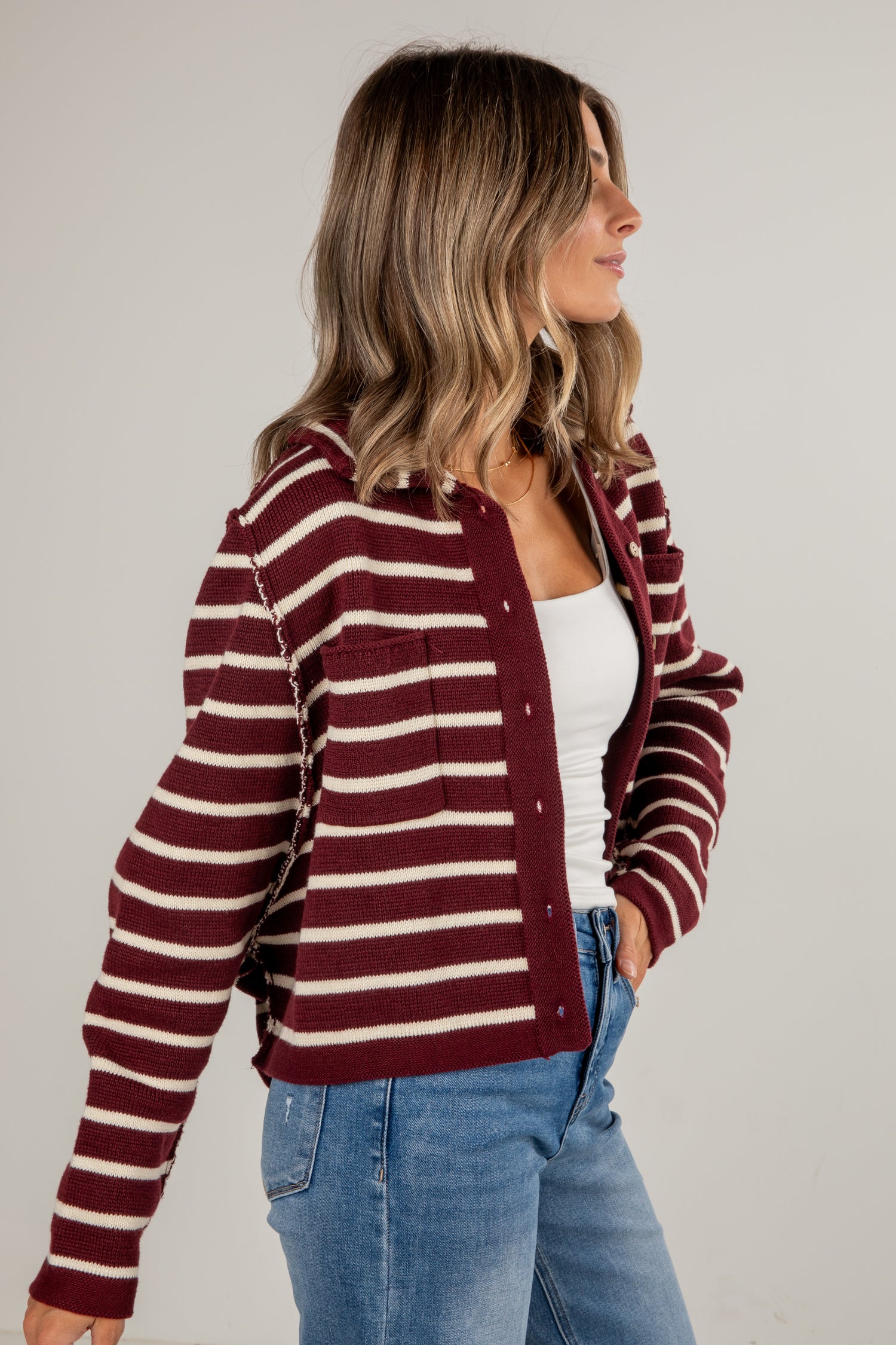 Woman wearing a maroon and white striped cardigan on a plain background