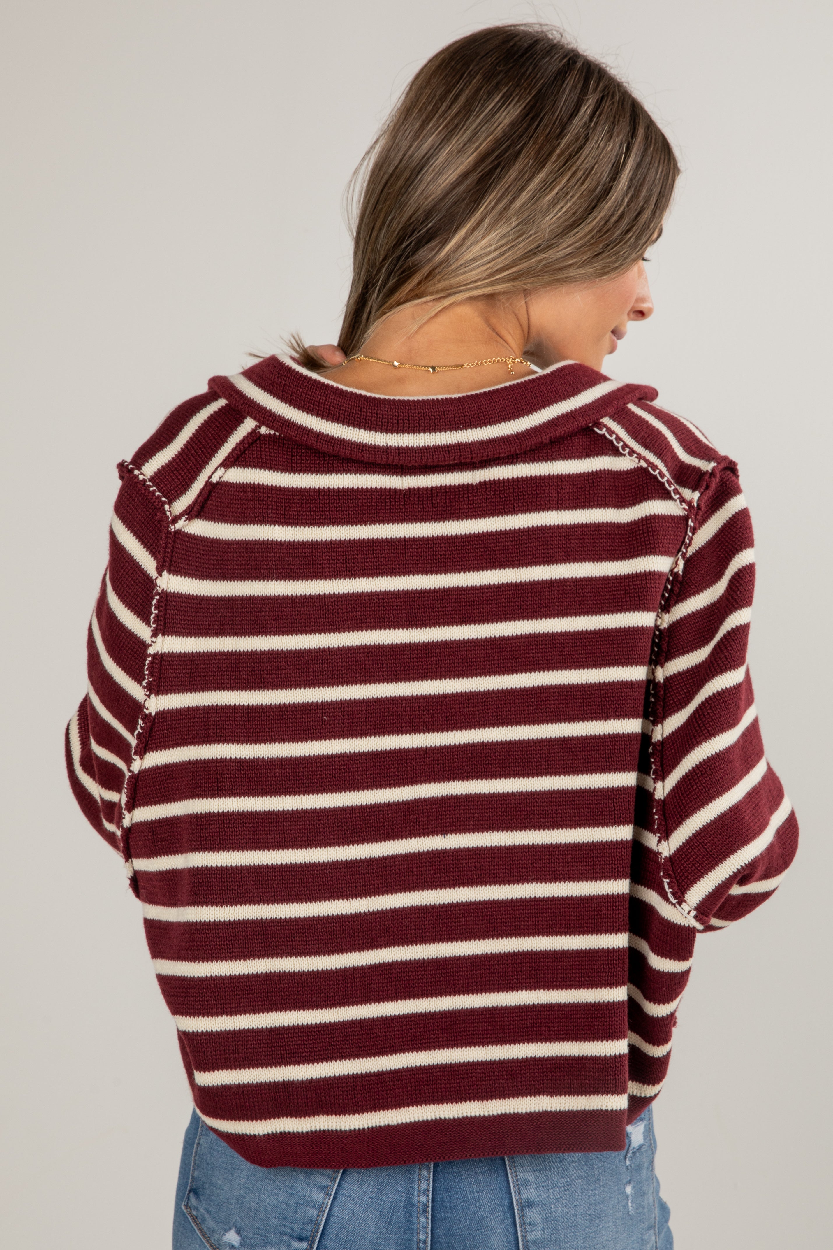 Woman wearing a maroon and white striped sweater on a plain background