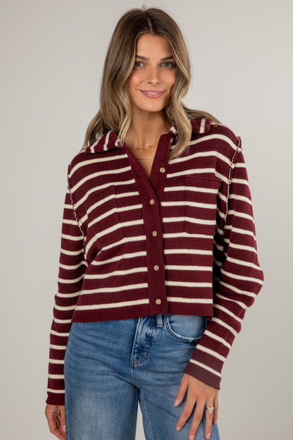 Woman wearing a maroon and beige striped sweater with blue jeans on a plain background