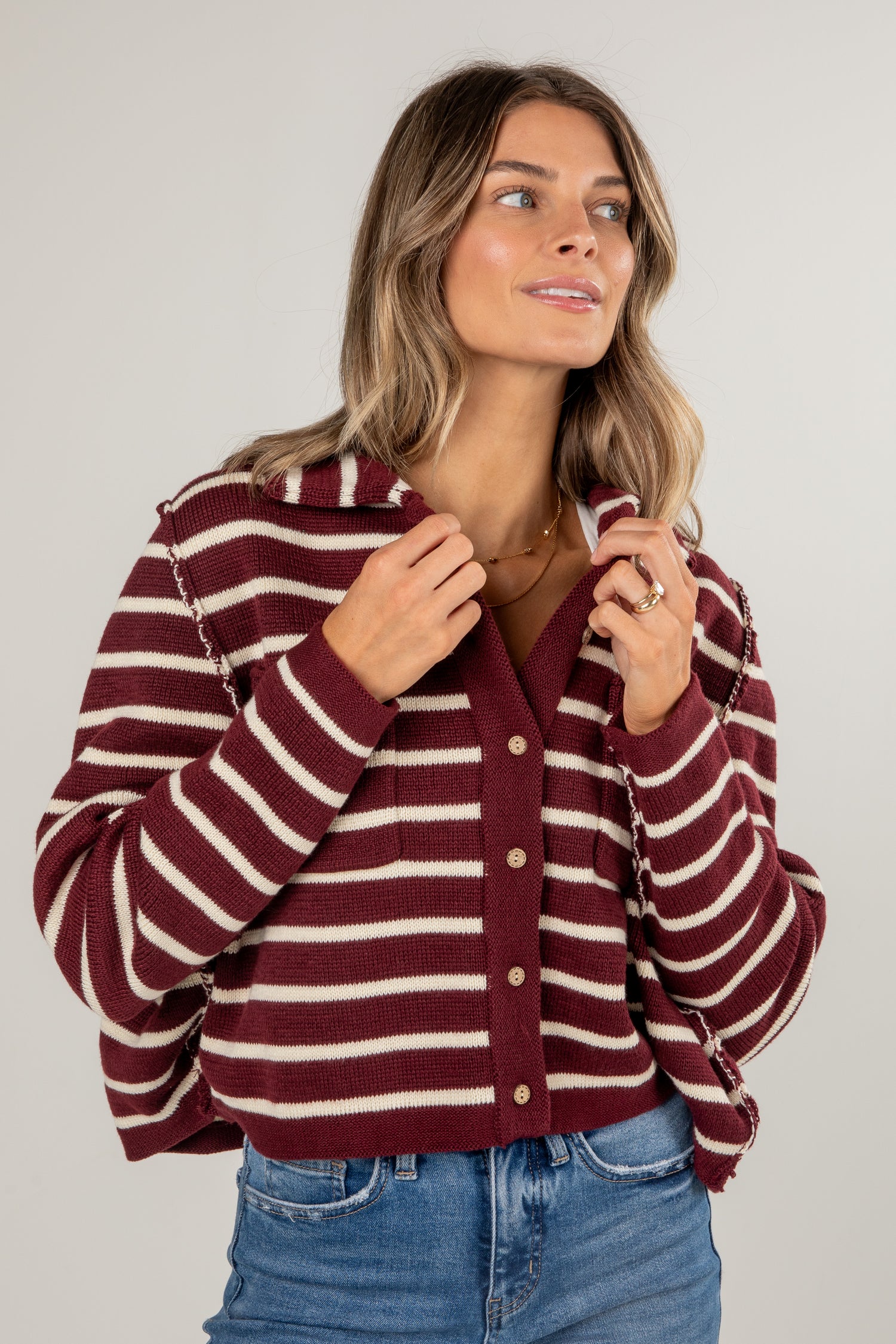 Woman wearing a maroon and white striped sweater with blue jeans on a plain background