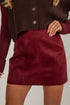 Maroon suede skirt worn with a brown ribbed sweater on a neutral background