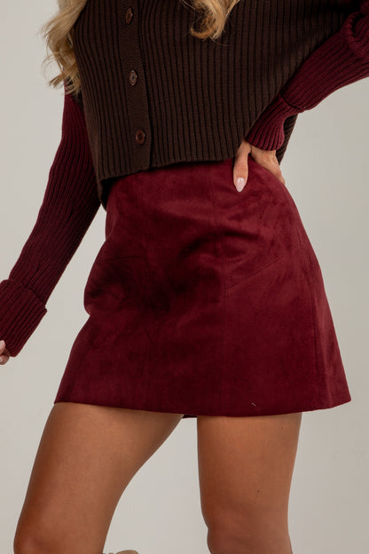 Person wearing a burgundy skirt and brown cardigan on a plain background