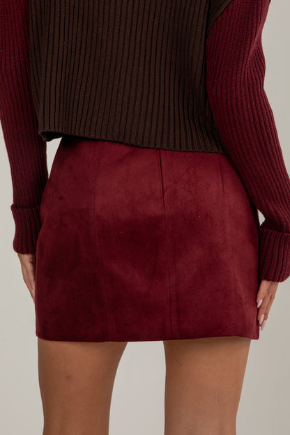 Burgundy suede mini skirt worn with a matching sweater on a neutral background