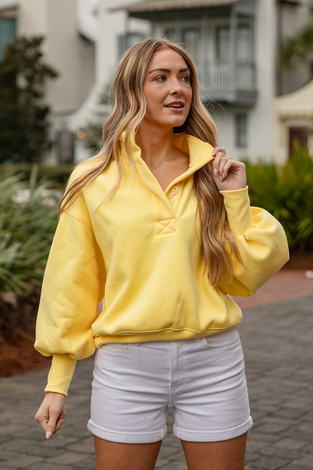 Woman wearing a yellow sweatshirt and white shorts outdoors.
