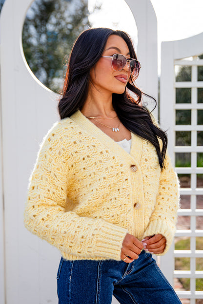 Woman wearing a light yellow cardigan and blue jeans standing outdoors.