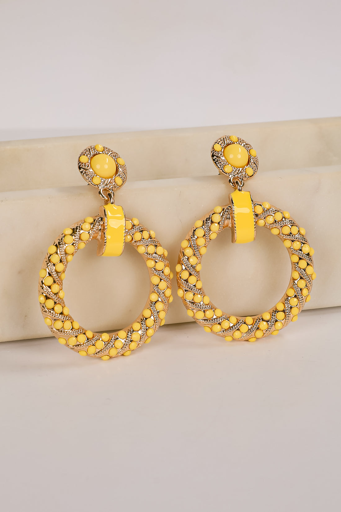 Yellow hoop earrings with intricate designs on a beige surface