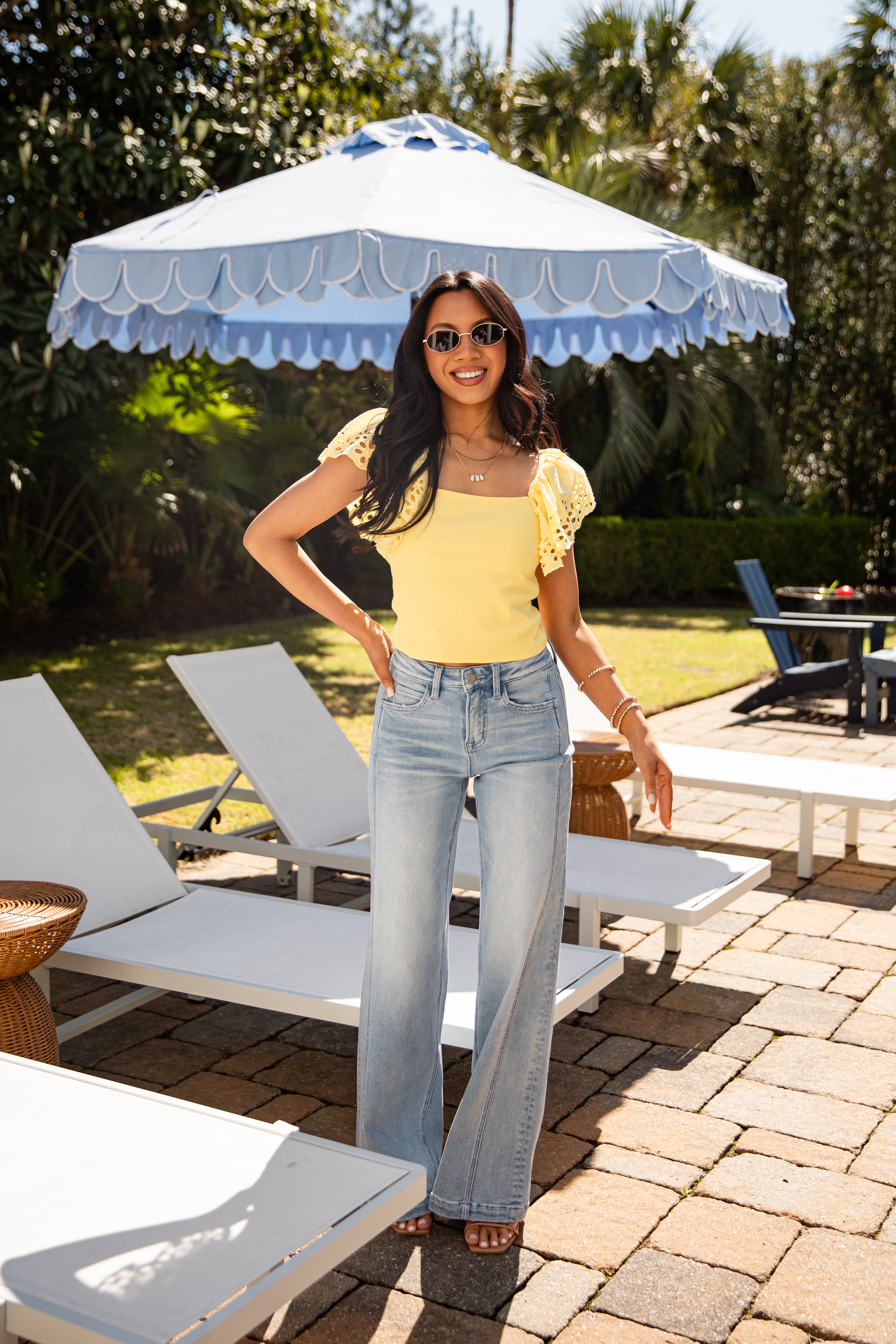 Woman in yellow top and jeans under umbrella shade.