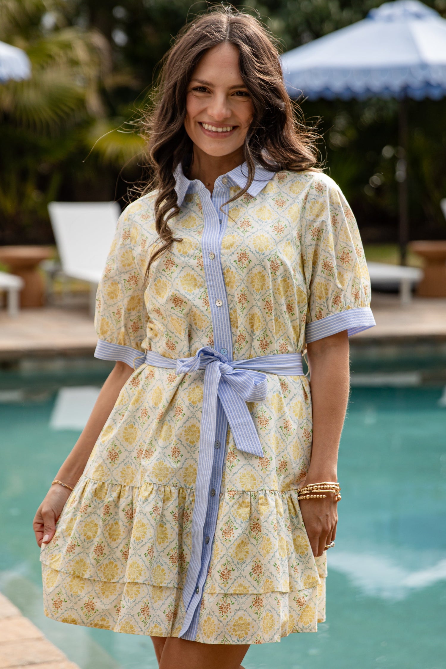 Woman wearing a yellow floral dress with a blue belt by a poolside.