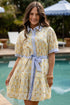 Woman wearing a yellow floral dress with a blue belt by a poolside.