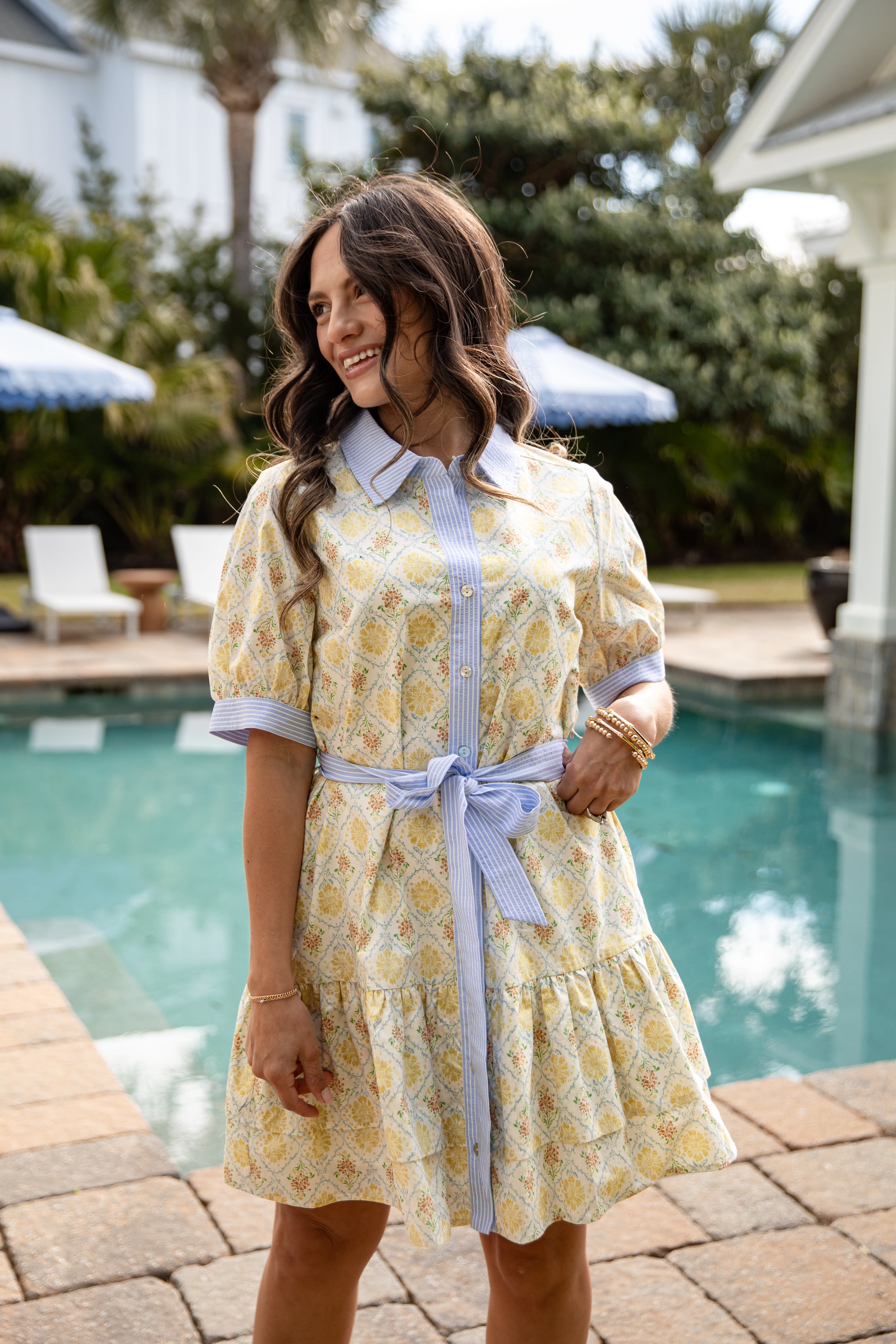 Woman in a yellow floral dress standing by a poolside.