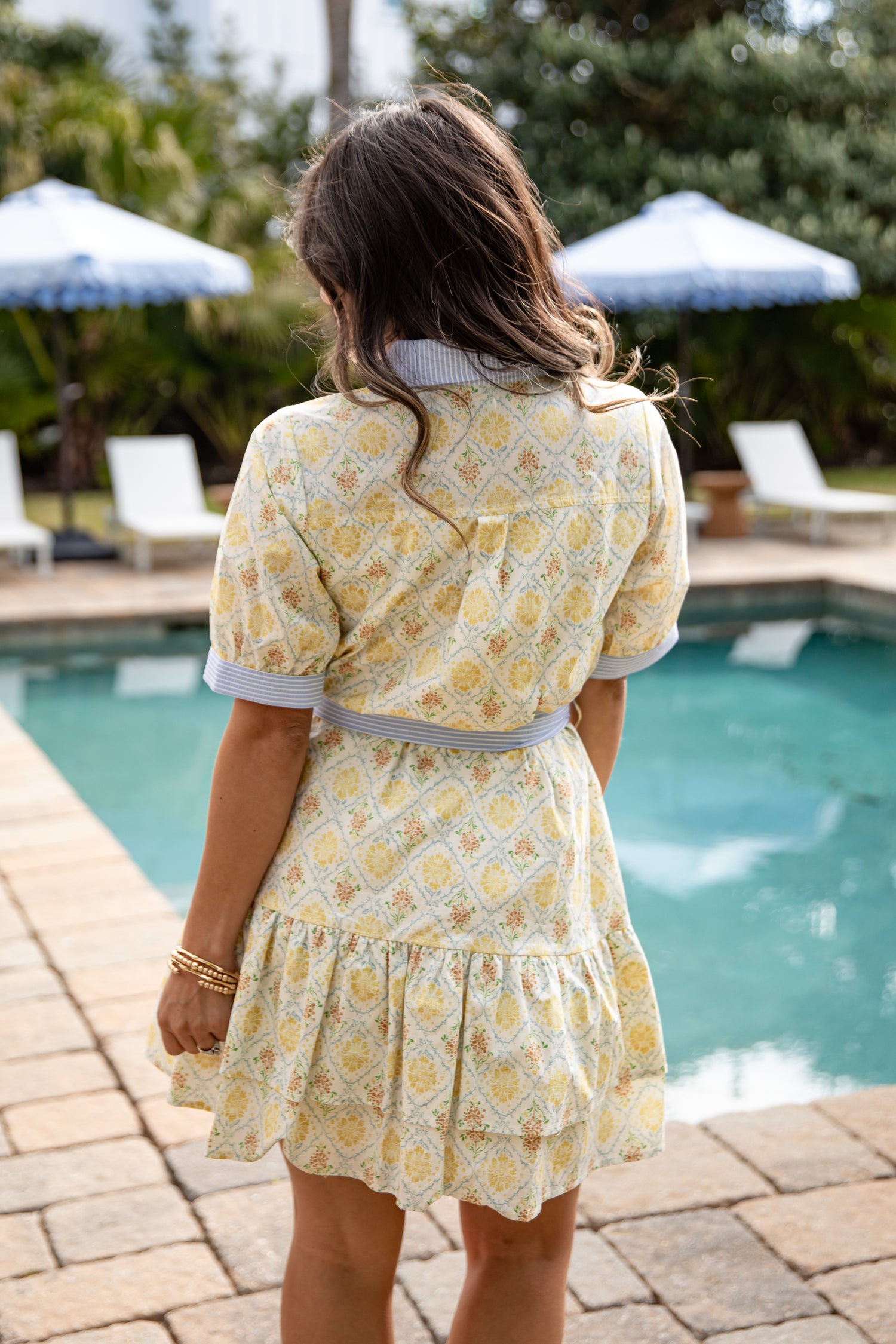 Woman in a yellow floral dress standing by a poolside.