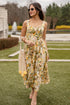 Woman in a floral dress standing on grass with a fountain in the background