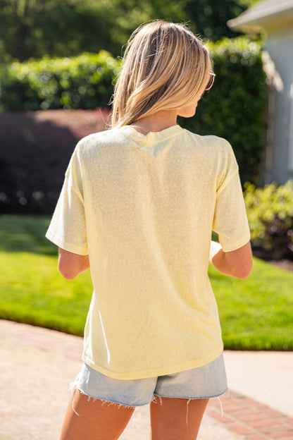 Person wearing a light yellow shirt and denim shorts standing outdoors.