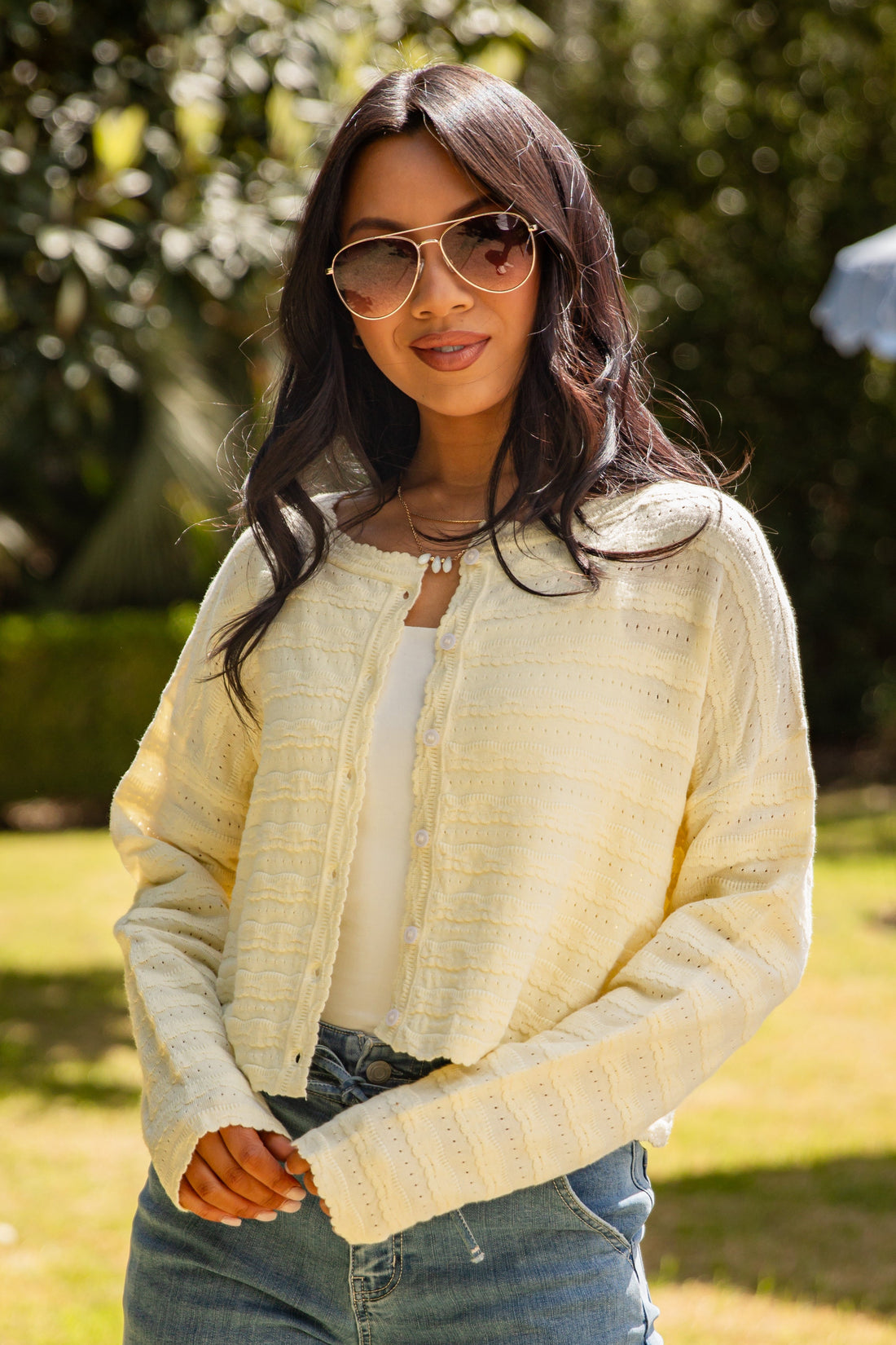 Woman wearing a light-colored cardigan and sunglasses outdoors