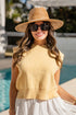 Woman wearing a yellow sleeveless top and white skirt with a straw hat and sunglasses by a pool.