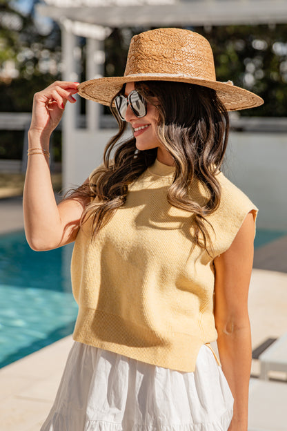 Woman wearing a straw hat and yellow top by a poolside