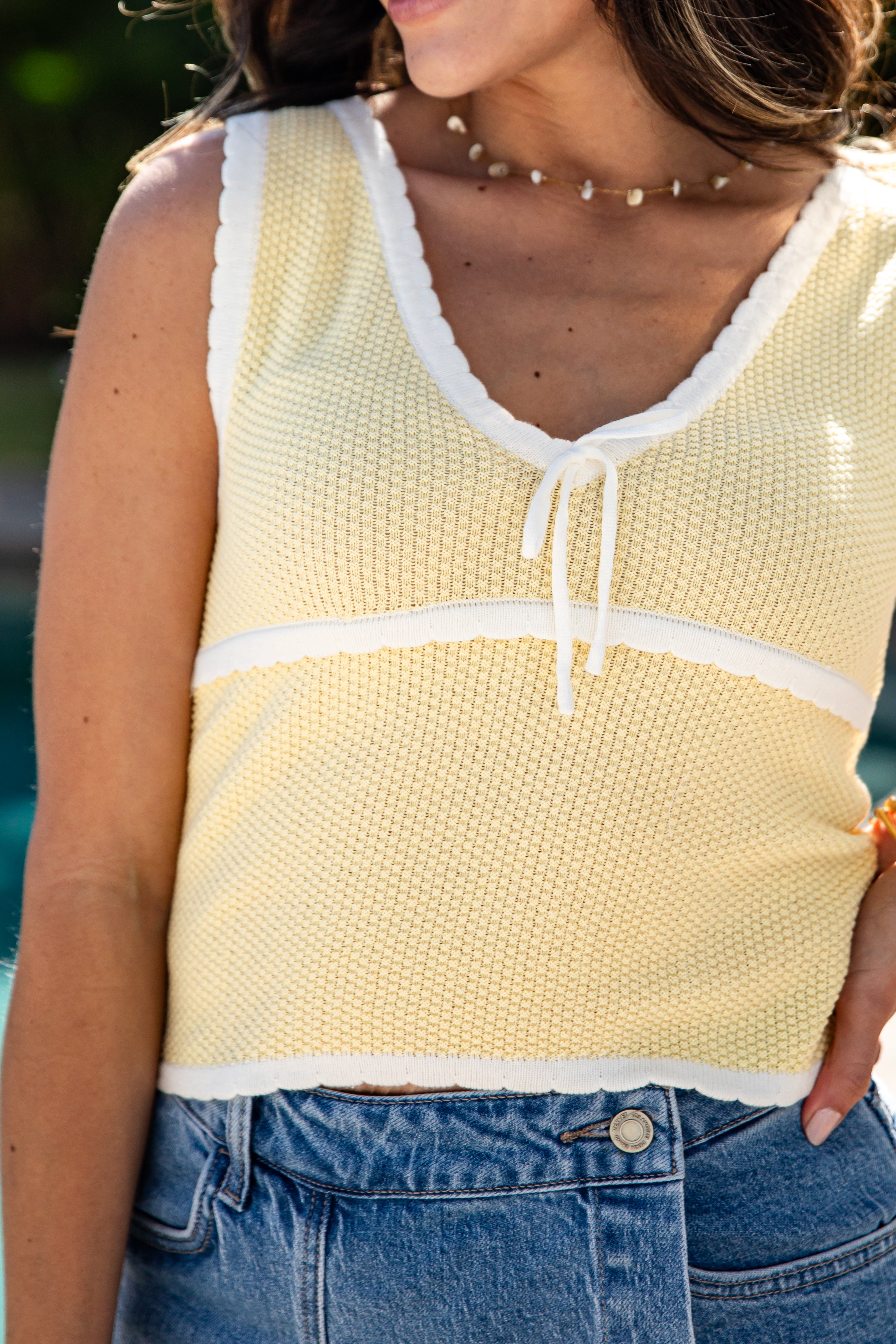 Woman wearing a yellow sleeveless top with white trim and blue jeans.