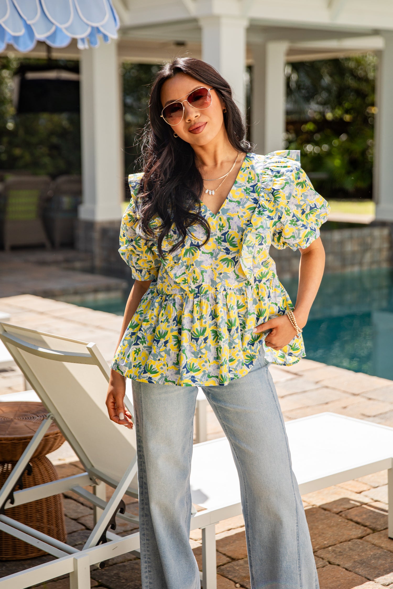 Woman in a floral top and light blue jeans standing by a poolside.