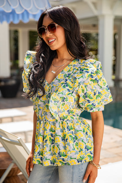 Woman wearing a floral blouse with lemon pattern by a poolside.