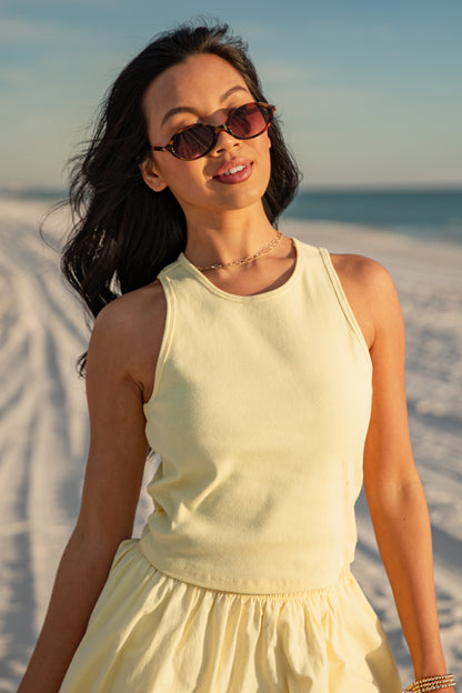 Woman in a yellow dress and sunglasses standing on a sandy beach.
