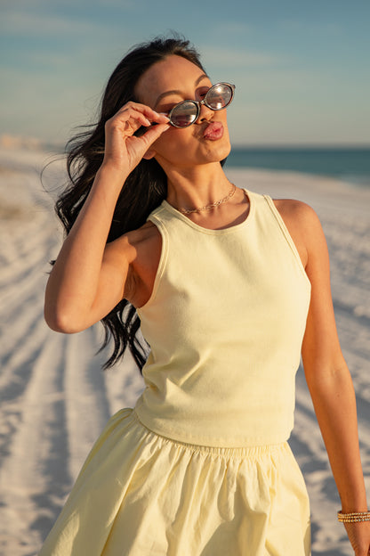 Woman in a yellow dress standing on a sandy beach with sunglasses