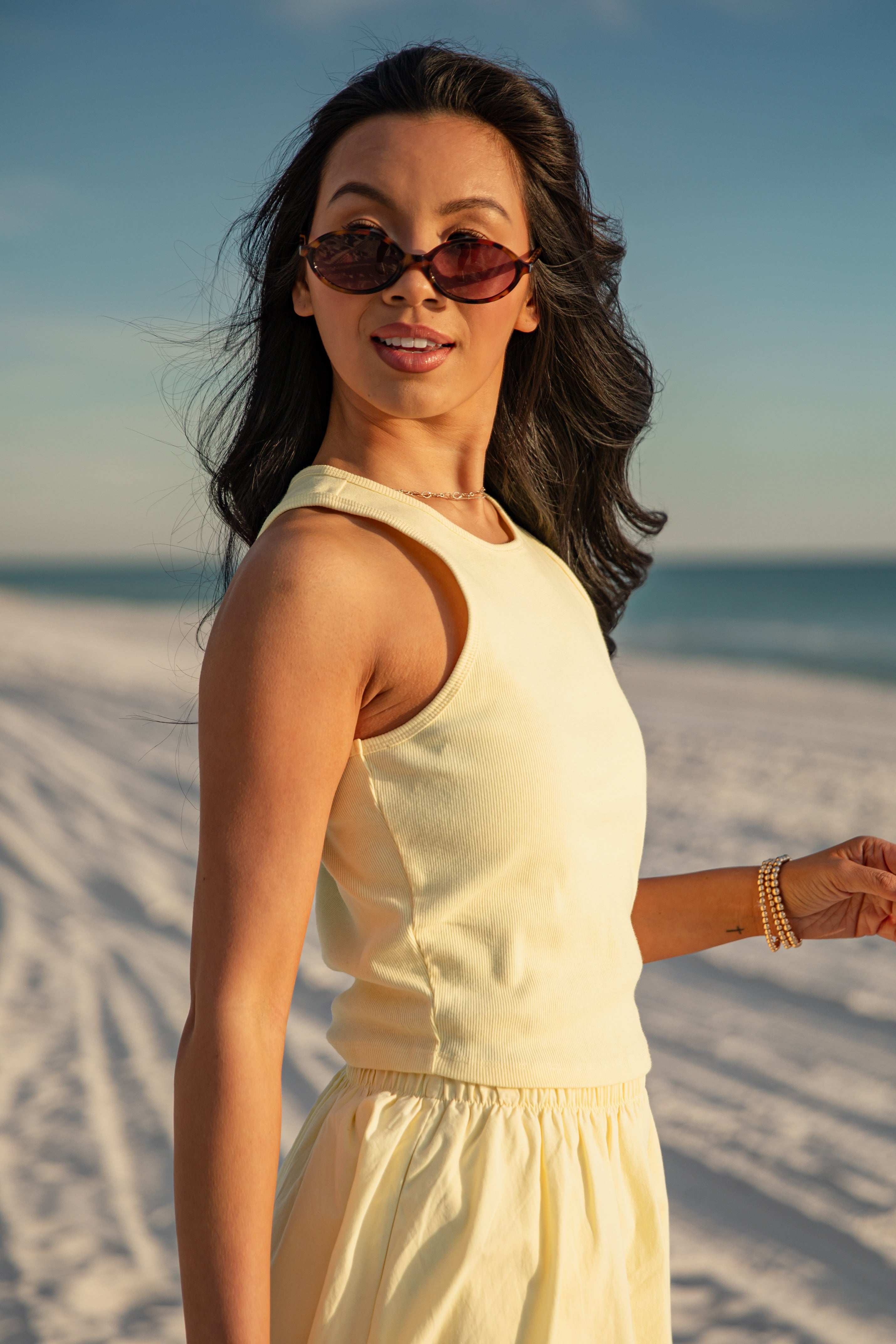 Woman in a yellow top standing on a sandy beach with ocean view