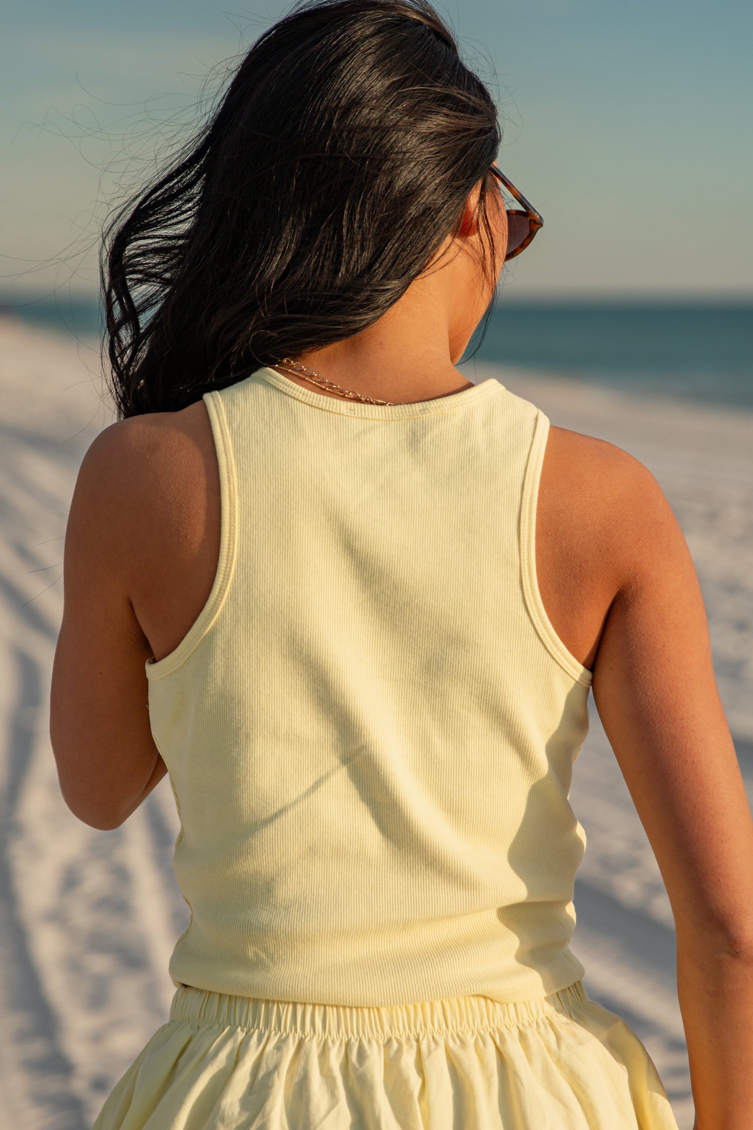 Woman in a yellow tank top and yellow skirt standing on a beach with ocean view