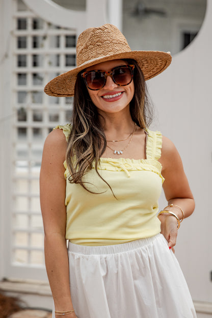 Woman wearing a yellow top, white skirt, and straw hat with sunglasses outdoors.