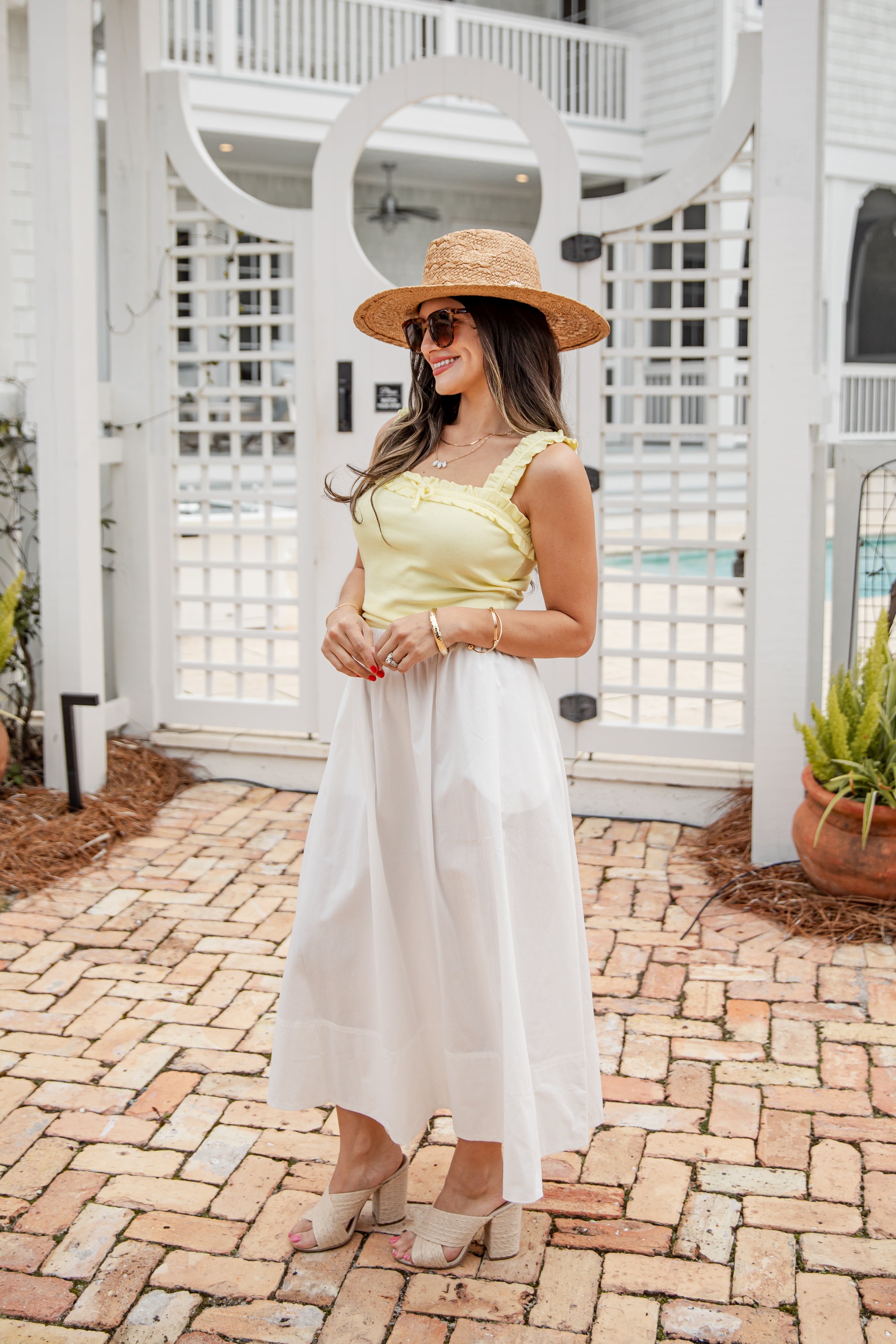 Woman in a yellow top and white skirt with a straw hat standing on a brick path.