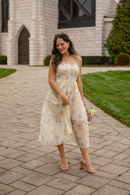 Woman in a floral dress standing on a paved walkway with a building in the background