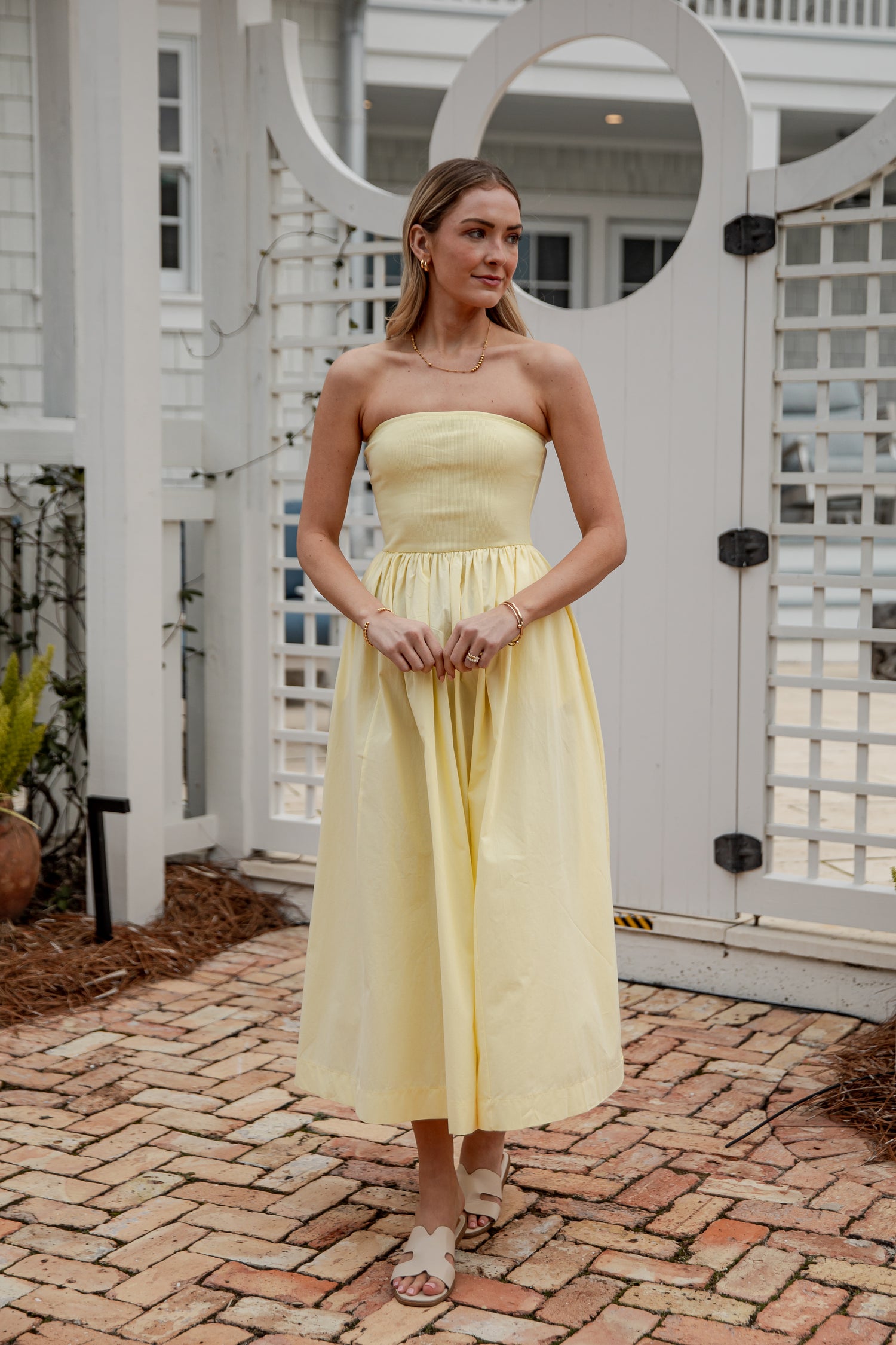 Woman in a yellow strapless dress standing on a brick patio.