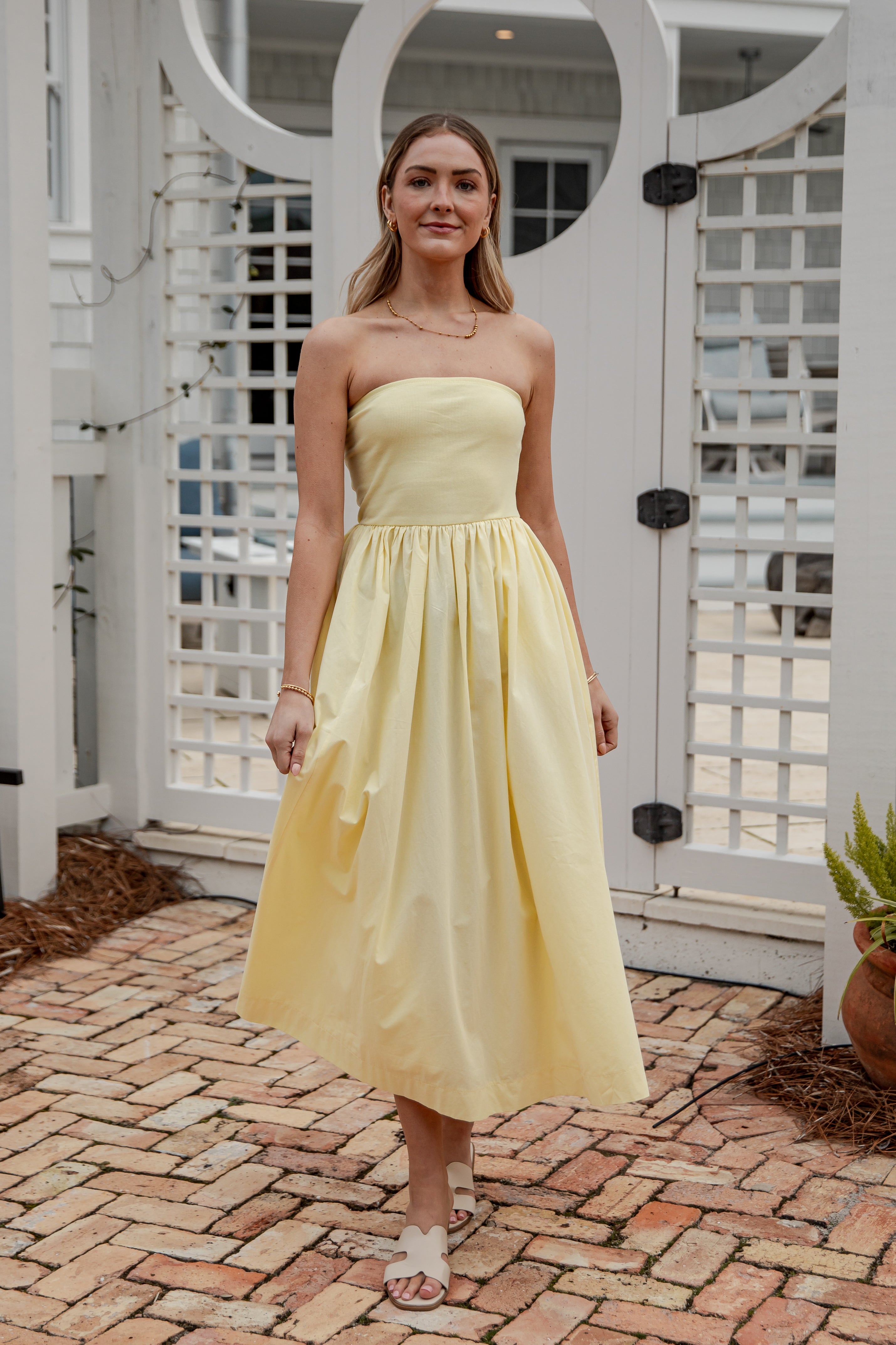 Woman in a yellow dress standing on a brick patio with white lattice background