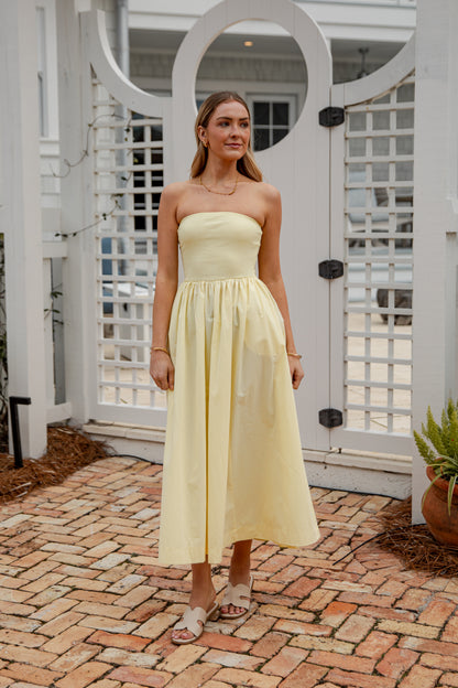 Woman in a light yellow strapless dress standing on a brick patio.