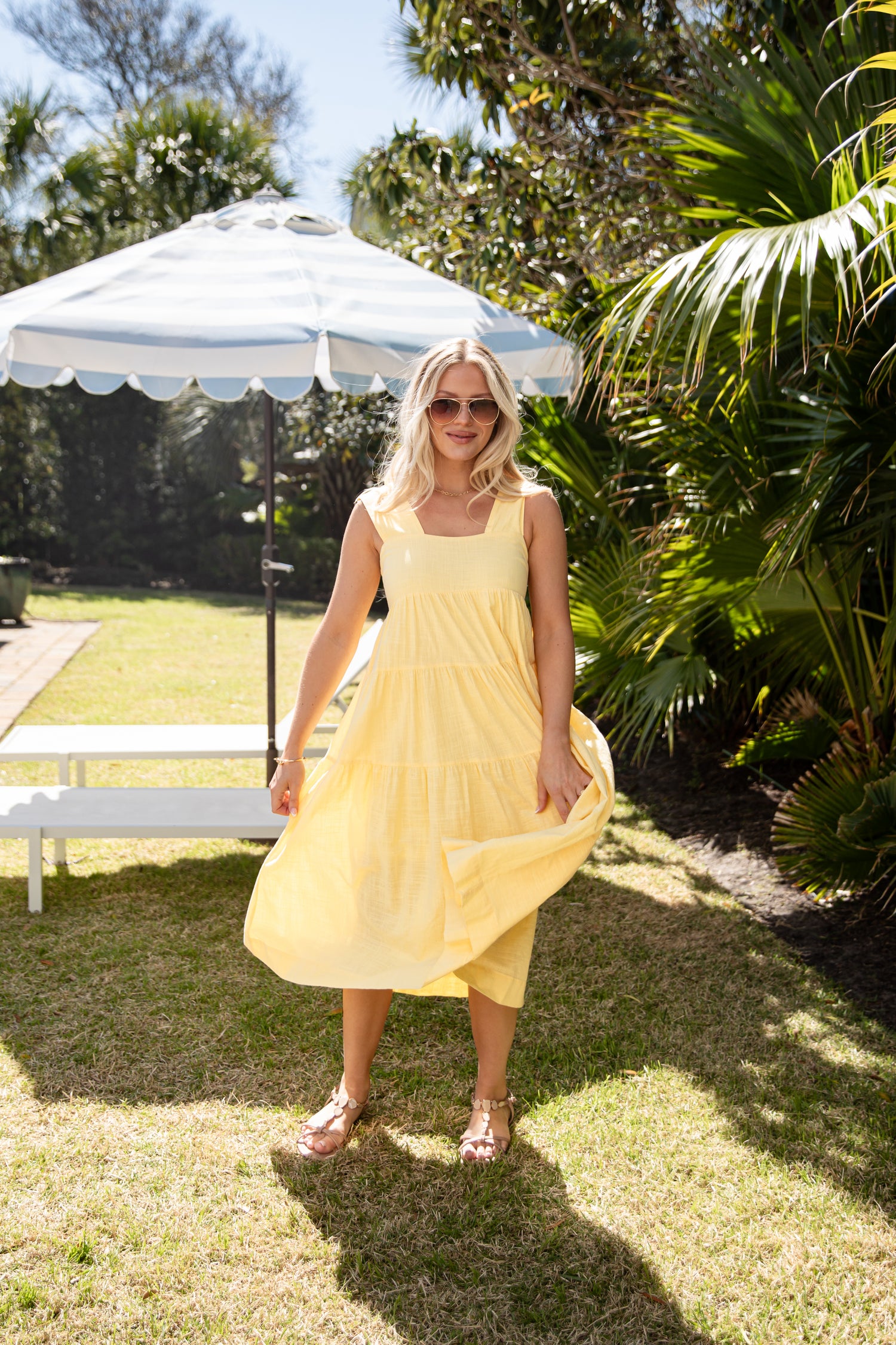 Woman in a yellow dress standing under a white umbrella in a garden setting