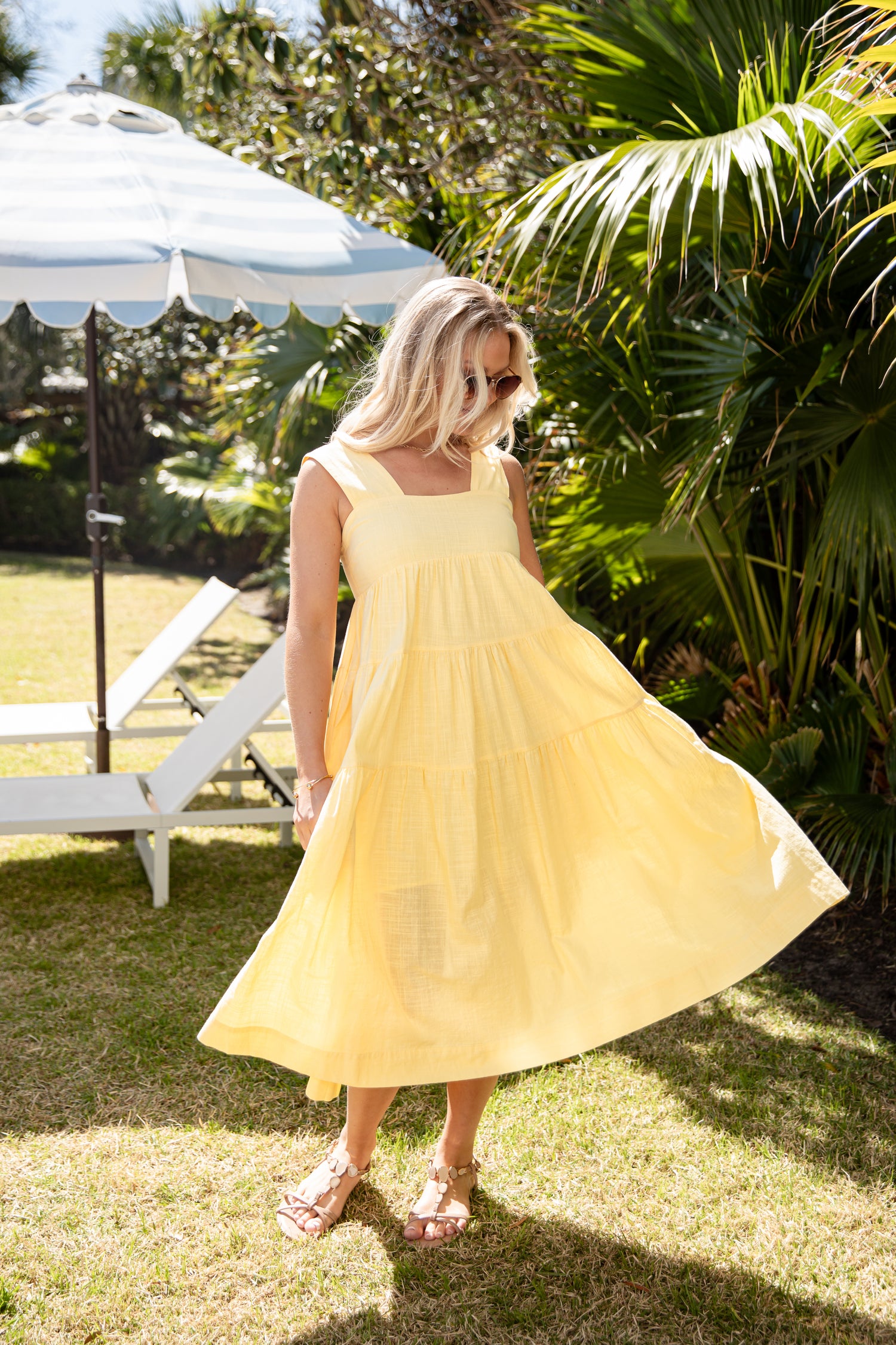 Woman in a yellow dress standing outdoors with greenery and a white umbrella in the background